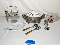Full lot photo showing all items on white background: covered casserole, ice bucket, serving utensils, glass basket, plates, nutcracker, and shakers.
