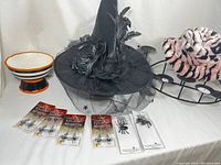 Photo showing the black witch hat with black spider web crown, four packages of plastic spider jewelry, the matte black 10-candle wrought iron candelabra, the Halloween candy bowl with black and orange stripes, and a pink and black furry hat.