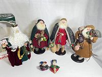Group of five Santa Claus figurines displayed including one in box and two small Santa ornaments on table.