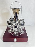 Full view of the wine decanter/carafe with 6 silver mercury luster wine glasses arranged on a chrome stand on wooden box.
