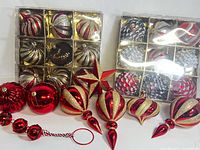 Photo showing boxed spherical ornaments in red, gold, and silver with swirl glitter design, loose finial ornaments, one red star, pine cone shapes, and string of small red balls.