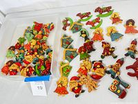 Wide view of collection of vintage handmade holiday dough ornaments including Santa, angels, houses, and rocking horses arranged on white surface with container.