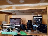 Photo showing Praktica LTL camera body, three lenses, two flash units, tripod, brown camera bag, and The Book of Photography book on a wooden shelf.