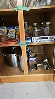 Shelf with glass canning jars, Bernardin snap lid boxes, meat grinder mounted on shelf edge, and boiling pots