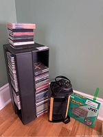 Full view of black plastic CD tower filled with over 100 CDs, JVC portable CD player with earphones, and the original JVC packaging box.