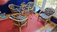 Four bamboo rattan chairs with floral upholstered cushions around a glass table (table excluded) on wooden floor and red carpet.