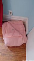 Folded pink wool blanket placed on wooden floor against a wall.