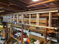 Full side view of the aluminum extension ladder resting horizontally on wooden racks in a basement storage area.