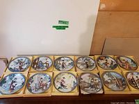 Twelve boxed hand painted plates arranged in two rows of six