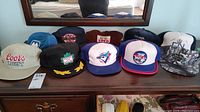 Photo showing all 8 baseball hats arranged on a wooden dresser under a mirror reflecting hats and background.