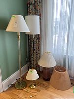 Set of four lamps including two floor lamps and two table lamps with shades, placed by a window on wooden floor.