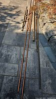 Metal pipes arranged on stone patio including various copper and steel pipes with fittings visible.