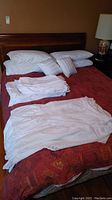 View of queen size bed with wooden headboard, white bedding including sheets, duvet, and bed skirt arranged on bed