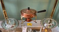 Front view of lot showing two silverplate serving dishes with lids and a central copper chafing dish with black handle sitting on a stand.