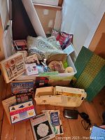 Wide view of lot showing Singer sewing machine, foot pedal, two large plastic bins filled with fabric, sewing books, magazines, patterns, threads, scissors, cutting mat, roll of vinyl and upholstery fabric.