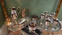 Photo showing two silverplate pitchers, a mug, six pewter goblets arranged on a silverplate tray along with bottle coasters