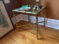 Front and left side view of the table showing the bamboo-style metal frame and glass top with decorative items on it.