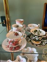 Photo showing all 5 teacups and matching saucers arranged on a glass shelf