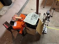 Overview of drill press stand, Craftsman router with stand, and router bit set on the floor in basement.