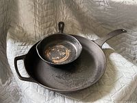 Two cast iron skillets placed one inside the other, showing surface wear and discoloration, on a light padded surface.