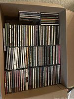 Box containing various CD jewel cases with multiple music genre titles visible on spines including country and oldies.