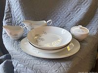 Two gravy boats, two bowls, two plates, and one lidded sugar bowl of white china with silver floral decoration and silver rims.