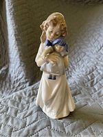 Glossy porcelain figurine of a girl holding a doll, cream-colored dress, detailed facial features and sculpting.