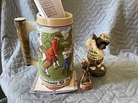 Photo showing Budweiser golf mug with certificate along with two golf figurines on a gray quilted fabric background