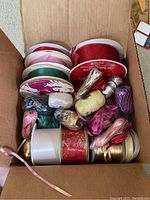 Top-down photo of a box with various ribbons in multiple colors and sizes along with decorative items.
