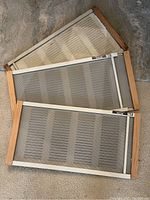 Photo showing two adjustable rain shield window screen inserts with wooden frames and metal mesh. The screens have adjustable top rails with measurement scales and locking mechanisms.