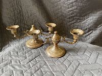 Photo showing two silver candle stick holders with two arms each, placed on a quilted gray surface.
