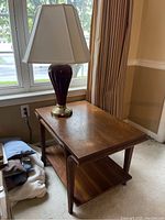 Wooden rectangular end table with purple ceramic lamp on top, window and curtains in background.