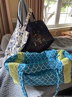 Photo shows three tote bags on a bed: the large blue and green Vera Bradley style duffel, black Italy souvenir tote with colorful embroidery, and cream and blue floral grocery tote.