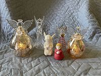 Photo showing six angel figurines arranged on quilted surface: two large mercury glass angels, one clear glass angel, two small ceramic angels, and one smaller striped glass angel.