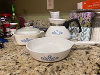 Photo of three vintage CorningWare Blue Cornflower pieces on kitchen counter: skillet, baker with lid, and tea kettle. Items show staining and signs of use.