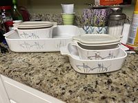 Photo of five white opaque CorningWare items on a kitchen countertop with blue iris floral design, including rectangular baking dish and multiple containers with lids.