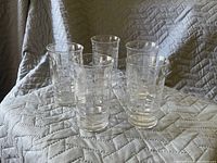 Set of five clear glasses with a geometric square textured pattern, arranged on a gray quilted surface.