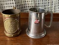 Birks pewter tankard on right and Mexico copper mug with Aztec calendar design on left side, shown together.