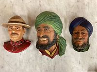 Three Bossons ceramic head sculptures displayed on flat surface showing wear, chips, and paint detail