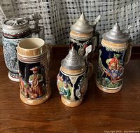 Photo of five ceramic beer steins, four with pewter lids, showing front views and relief artwork
