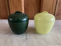 Front view showing the two lidded dishes side by side, one green and one yellow, highlighting their rounded shape and lid handles.