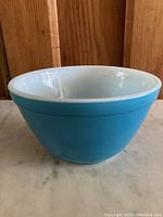 Side profile of vintage blue Pyrex 401 mixing bowl showing the solid blue exterior and white interior with a wide rim, placed on marble surface with wooden background.