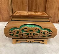 Side view of wooden Asian box with carved design and green fabric underneath