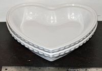 Two stacked white ceramic heart-shaped baking pans with ruler showing dimension approx. 9-10 inches across.