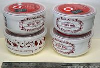 Four stackable round white porcelain covered bowls with Christmas-themed red and brown decorations and clear plastic lids, shown with a ruler for size reference.