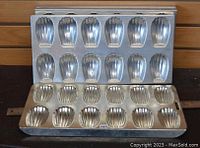 Four metal madeleine cookie pans arranged showing the shell-shaped cavities for baking. Used condition with metallic finish.