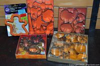 Photo showing multiple autumn themed cookie cutters in various packaging and boxes, including a gingerbread man cutter with an orange plastic holder and sets of metal leaf and pumpkin shapes.