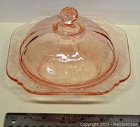 Pink depression glass butter dish with lid on a white background with measurement scale.