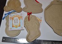 Five clay molds and a small recipe book arranged on surface with measuring ruler showing size.