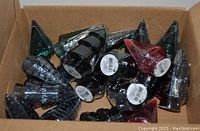 Glass Christmas tree figurines in assorted colors inside an open cardboard box.